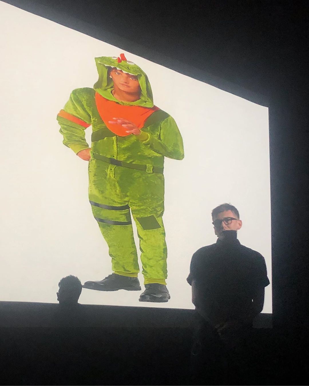 person standing in front of projected image of a thumbnail from a halloween costume catalog. the signified of the costume is unclear