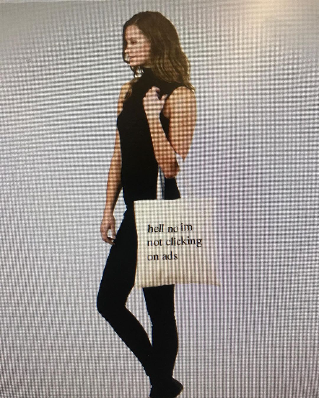 catalog image of a female model holding a tote bag with 'hell no im not clicking on ads' printed in large times new roman font